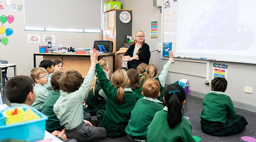 students in the classroom, eagerly raising their hands to answer a question